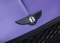 Close-up of a black Bentley emblem on the hood of a Violette Color Continental GTC Speed, with part of the front grille visible below.