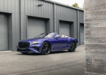 A bespoke Bentley Continental GTC in the striking Violette color is parked in front of a row of gray garage doors on a paved surface.