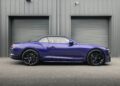 A blue Bentley Continental GTC Speed convertible with a black soft top is parked in front of two closed gray garage doors on a paved surface, its stunning hue reminiscent of the distinctive Violette Color.