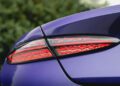 Close-up of the rear taillight of a Bentley Continental GTC Speed in striking Violette color, showing the illuminated red light with a textured pattern, set against a blurred green background.