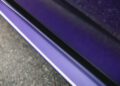 Close-up of the lower side panel of a Bentley Continental GTC Speed in Violette Color, showcasing the glossy paint and a striking white accent line beside a rough asphalt surface.