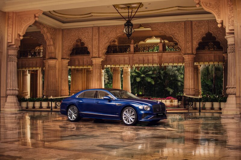 A blue Bentley luxury sedan parked on a polished floor under an ornate, arched pavilion with decorative columns and lush greenery, highlighting the brand’s growing Indian presence and elegance in new showrooms.