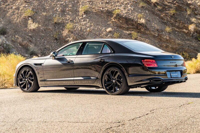 A black luxury sedan from the First Ombré by Mulliner Collection is parked on a paved road near a rocky, dry hillside under sunlight—one of three bespoke commissions arriving at Bentley Rancho Mirage.