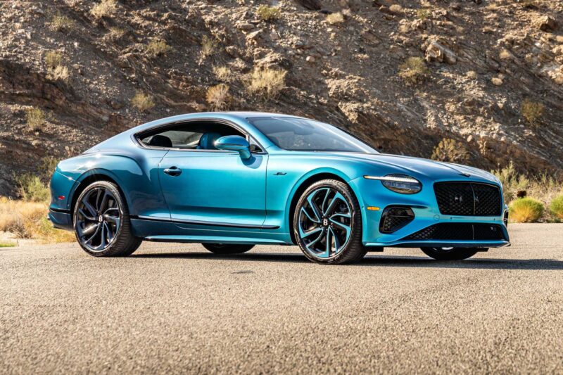 A blue luxury coupe car parked on a paved road with rocky hills in the background, featuring the First Ombré by Mulliner Collection, which arrives at Bentley Rancho Mirage with three bespoke commissions.