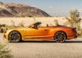 A metallic orange convertible sports car, part of the First Ombré by Mulliner Collection, is parked on a desert road with mountains in the background—one of three bespoke commissions arriving at Bentley Rancho Mirage.