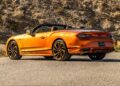 An orange Bentley convertible parked on a paved road near a rocky hillside, shown from the rear side angle—part of the First Ombré by Mulliner Collection Arrives at Bentley Rancho Mirage With Three Bespoke Commissions.