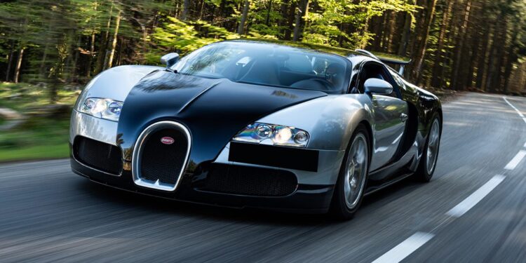 A black and silver Bugatti Veyron, featuring the advanced Chassis 5.0, speeds along a winding road through a lush, forested landscape.
