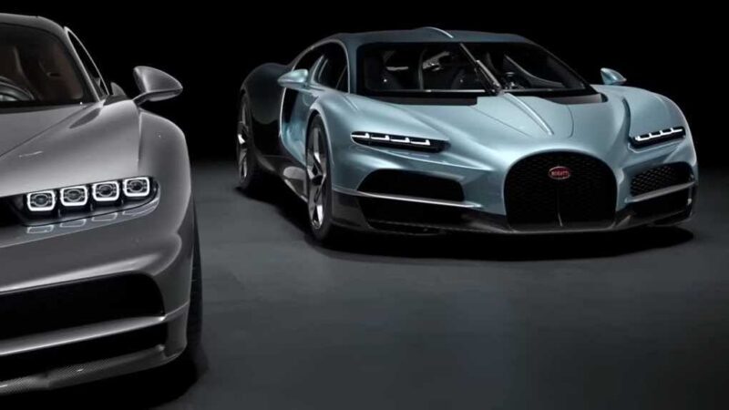 Two luxury sports cars, one silver and one light blue, are parked side by side in a dark studio setting, illustrating how form, function, past and the future came together in the Bugatti Tourbillon.