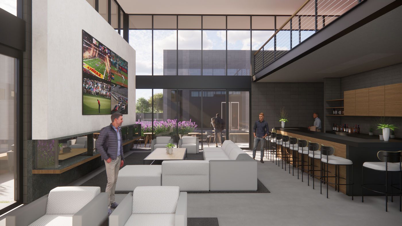 Modern lounge area with white sofas, a bar, and large windows; several people are present, and two TVs display sports on the wall.