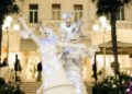 Three street performers in elaborate white costumes and face paint pose dramatically before an elegant, well-lit building with palm trees—capturing the festive spirit of the Modena Cento Ore 25th Anniversary, held Oct. 5-10.
