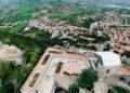Aerial view of a historic hilltop fortress with red-roofed buildings, surrounded by green fields and a sprawling town below—capturing the charm of Modena Cento Ore's 25th Anniversary, Oct. 5-10.