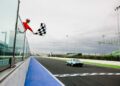 A race official waves a checkered flag as a classic car crosses the finish line on a racetrack under a cloudy sky during the Modena Cento Ore 25th Anniversary, held from Oct. 5-10.