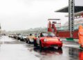 A lineup of classic race cars waits on a wet pit lane at the Modena Cento Ore, with a race official in an orange rain suit standing nearby during the 25th Anniversary event, Oct. 5-10.