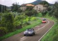 Three vintage cars drive along a winding rural road surrounded by greenery, with stone houses and hills in the background during the 25th Anniversary Modena Cento Ore, held Oct. 5-10.