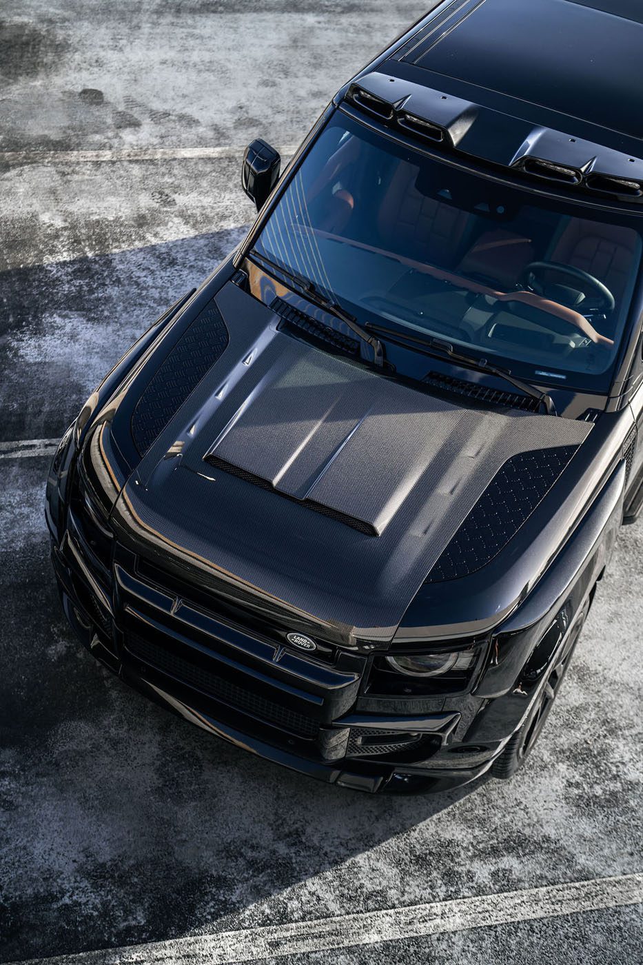 A black SUV with a custom matte hood and details, inspired by ECD Auto Design, is parked in an outdoor lot, viewed from above at an angle.
