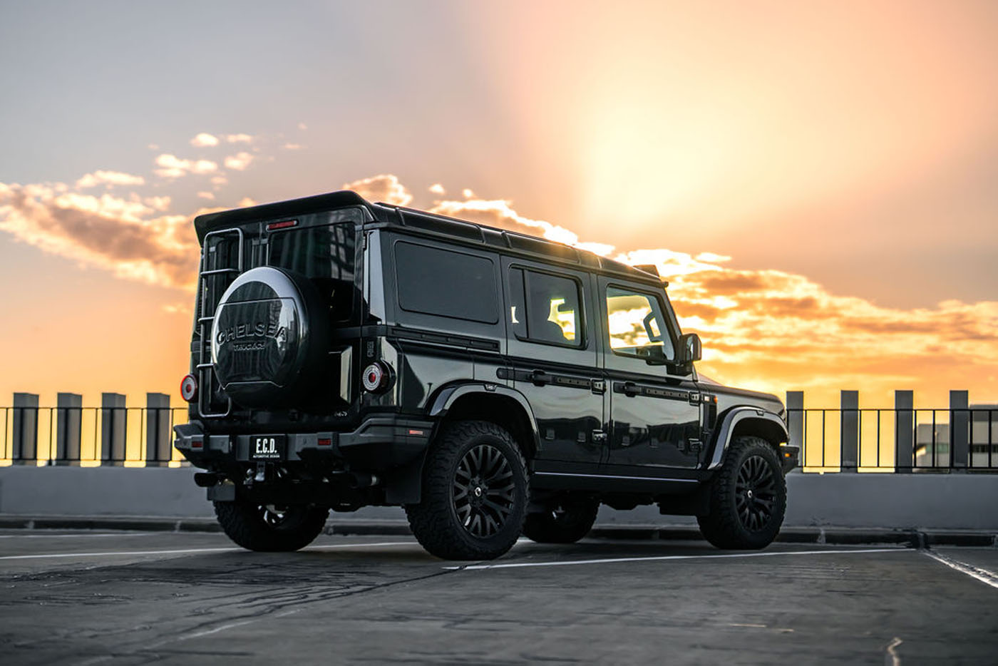 Black SUV parked on a rooftop with the sun setting in the background, casting a warm glow and long shadows on the concrete—an unmistakable statement of style by Chelsea Truck Company.