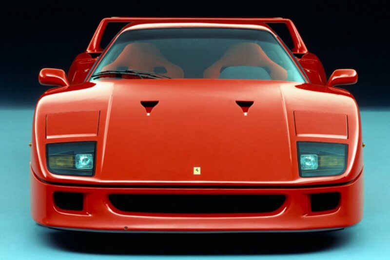 Front view of a red Ferrari F40 sports car, highlighting its headlights, hood vents, and aerodynamic design against a plain background—perfect for a Comparison: Ferrari F40 Vs Ferrari F50.