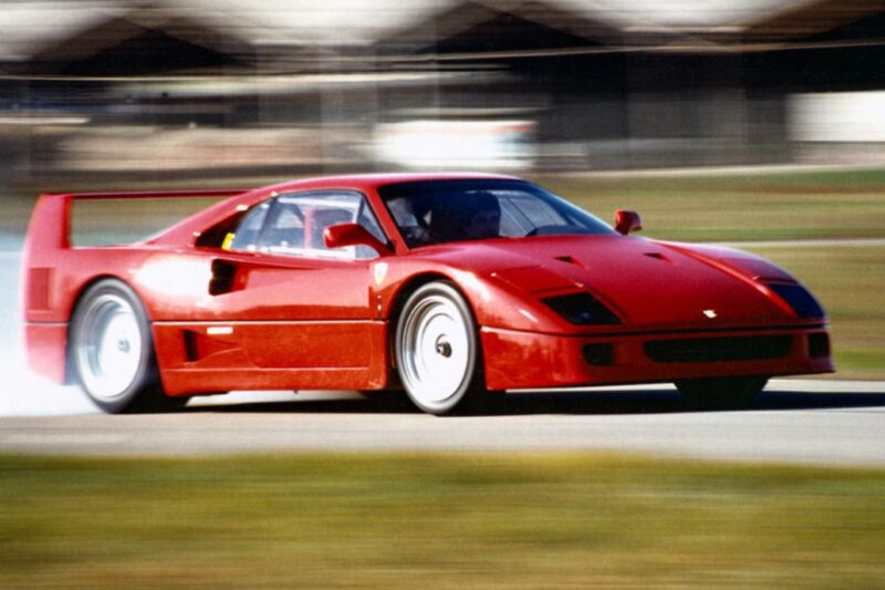 A red Ferrari F40 sports car skids on a racetrack, smoke billowing from the rear tires and a blurred background—showcasing its power in a thrilling moment. Comparison: Ferrari F40 Vs Ferrari F50 highlights the F40’s raw, iconic edge.
