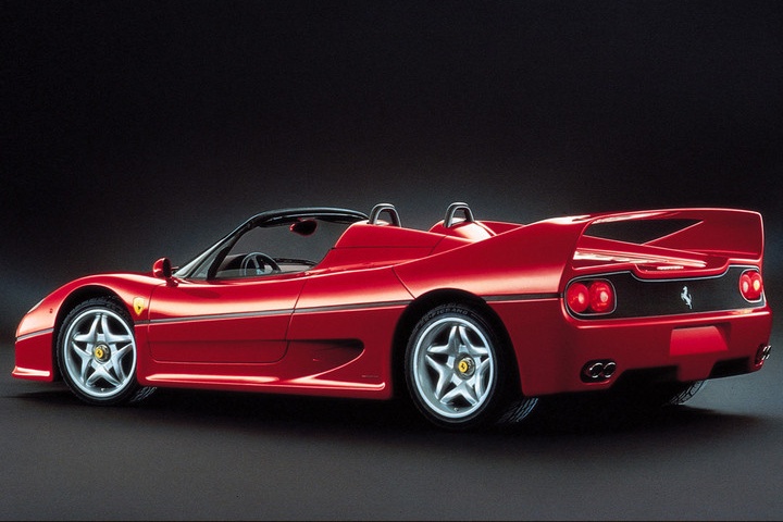 A red convertible sports car with a rear spoiler, viewed from the back left side against a dark background, reminiscent of the iconic lines seen in the Ferrari F40 vs Ferrari F50 comparison.