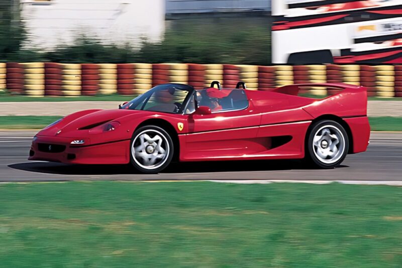 A red Ferrari F50 convertible sports car drives on a racetrack with red and yellow barriers in the background, showcasing its style for those considering the ultimate Comparison: Ferrari F40 Vs Ferrari F50.
