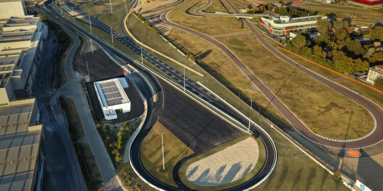 Aerial view of the Ferrari e-Vortex Test Track, a large, winding test track with multiple curves and paved roads, surrounded by grassy areas and nearby buildings.