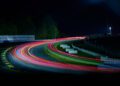 Long-exposure photo of the Petit Le Mans race track at night, with colorful light trails curving around a bend, illuminated signs, and a dark sky—Rolex signage glows in the background.