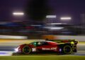 A red and black Cadillac race car with number 31 and Whelen branding speeds along the racetrack at night during Petit Le Mans, lights and Rolex signage blurred in the background.