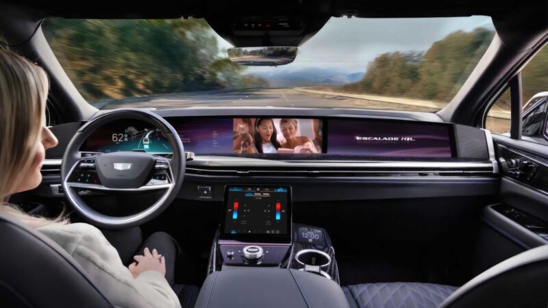 A woman sits in the driver’s seat of a self-driving car, hands off the wheel, as the vehicle navigates a highway; multiple digital screens display driving data and entertainment—foreshadowing GM’s Next Big Leap: Conversational AI in 2026 Eyes-Off Driving from 2028.