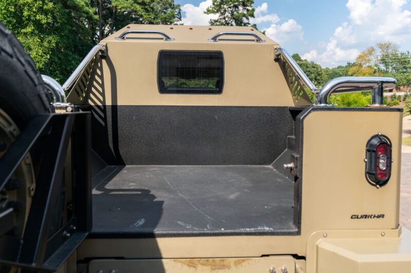 The image shows the empty rear cargo bed of a tan 2020 Terradyne Gurkha, a street-legal armored vehicle with metal rails, a small rear window, and a "Gurkha" badge on the tailgate.