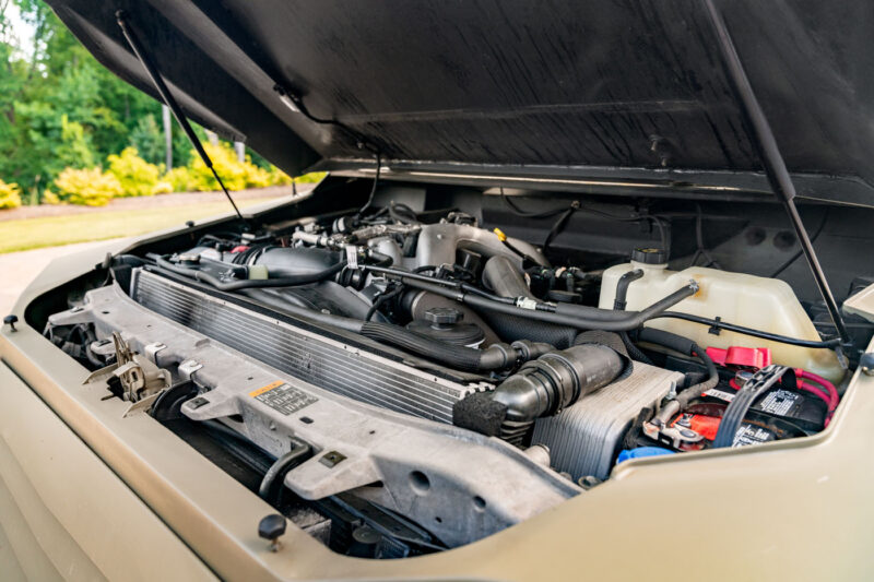 Close-up view of a Terradyne Gurkha engine compartment with the hood open, showing various street-legal engine components, hoses, and the battery.