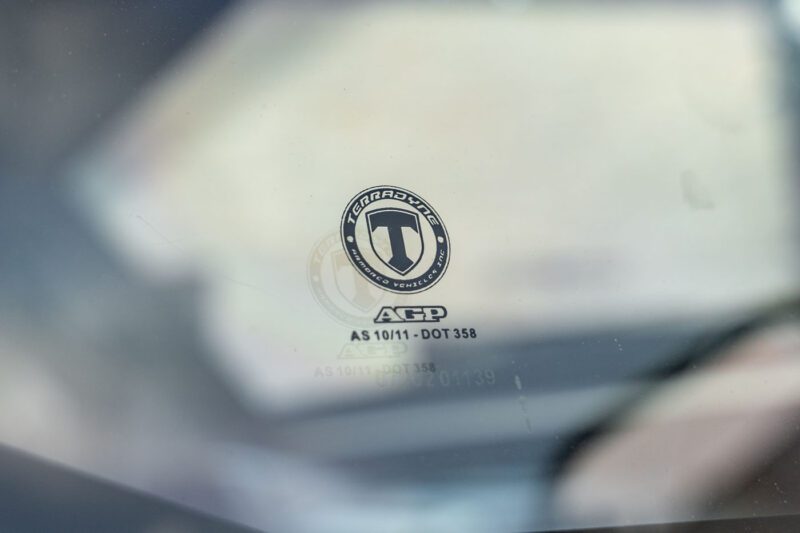 Close-up of a Terradyne Gurkha windshield displaying a "Tempered" certification logo with the text "AGP AS 10/11 - DOT 358" printed below it. This street-legal vehicle is now available for sale.