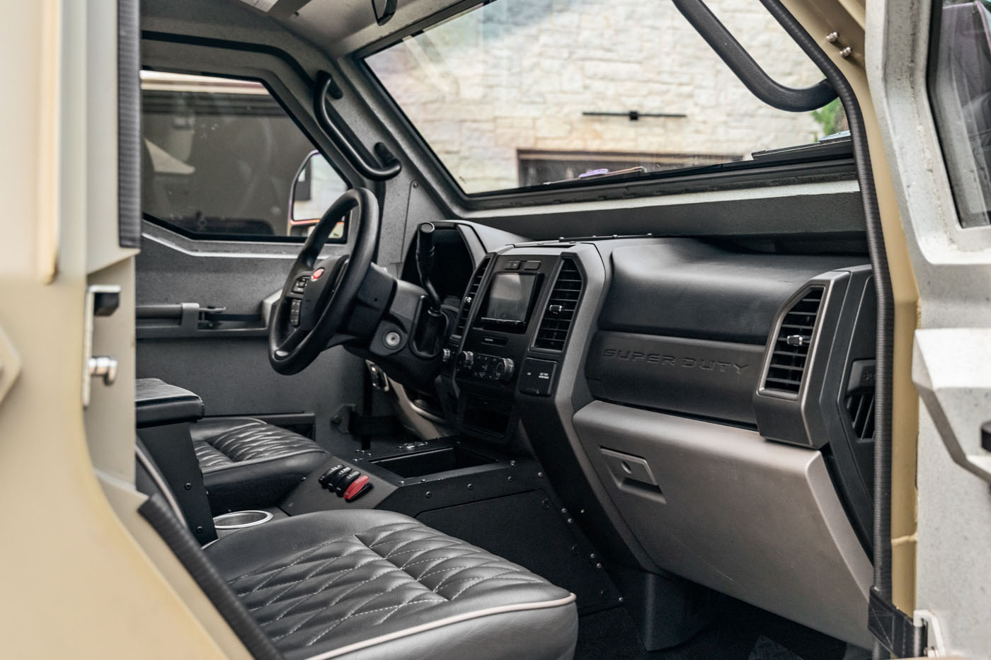 Interior view of a street-legal Terradyne Gurkha for sale, showcasing quilted leather seats, a steering wheel, and a dashboard labeled "Super Duty," all designed with sturdy, utilitarian features.