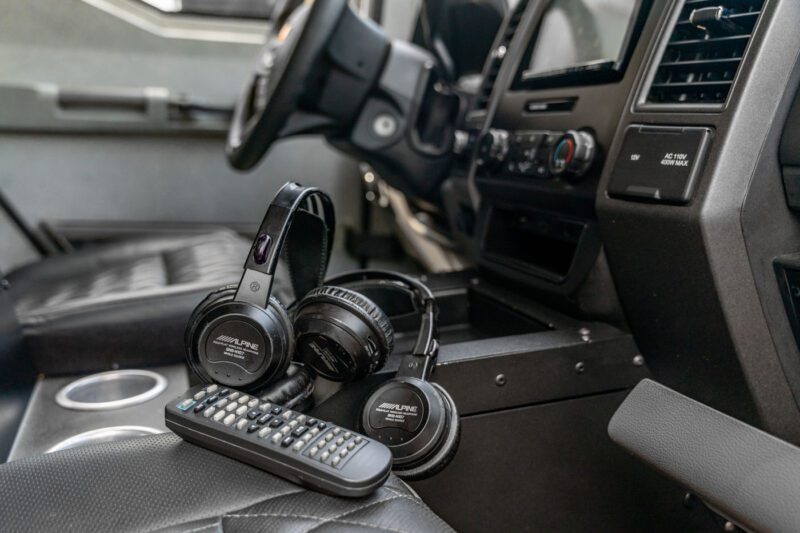 Two Alpine wireless headphones and a remote control rest on the center console of a street-legal Terradyne Gurkha for sale, showcasing premium in-vehicle entertainment.