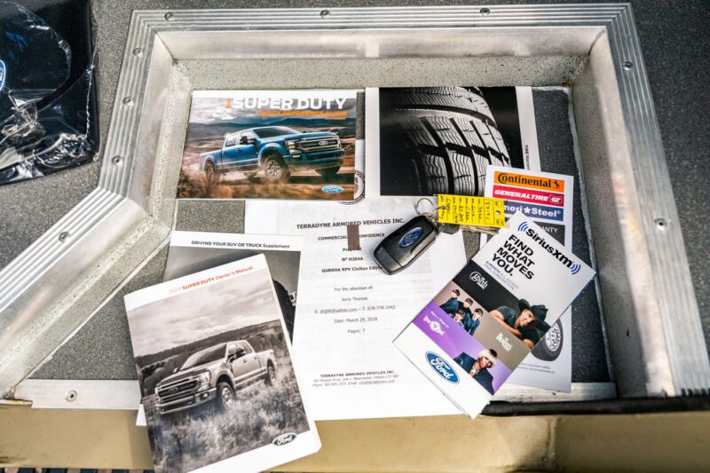 A collection of Ford truck documents, brochures, a Continental tire pamphlet, a key fob, a yellow tag, and a SiriusXM leaflet—essentials for approaching the street-legal fortress Terradyne Gurkha for sale—with everyday manners—arranged on a metal surface.