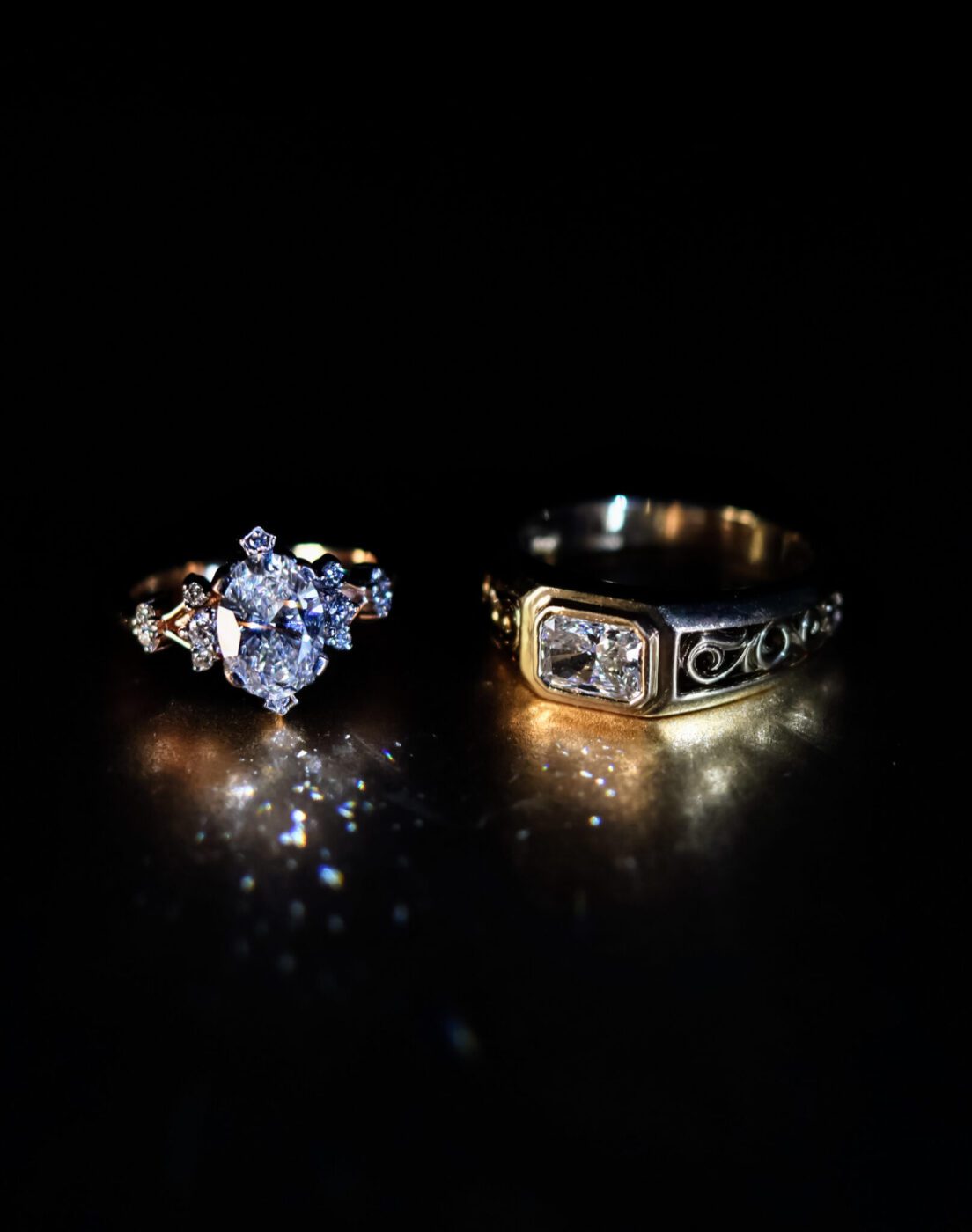 A close-up of two diamond rings on a dark surface from AviNika Jewelry: one with a central round diamond and side stones, the other with a rectangular diamond and engraved band—timeless heirlooms destined to become rare legacies.
