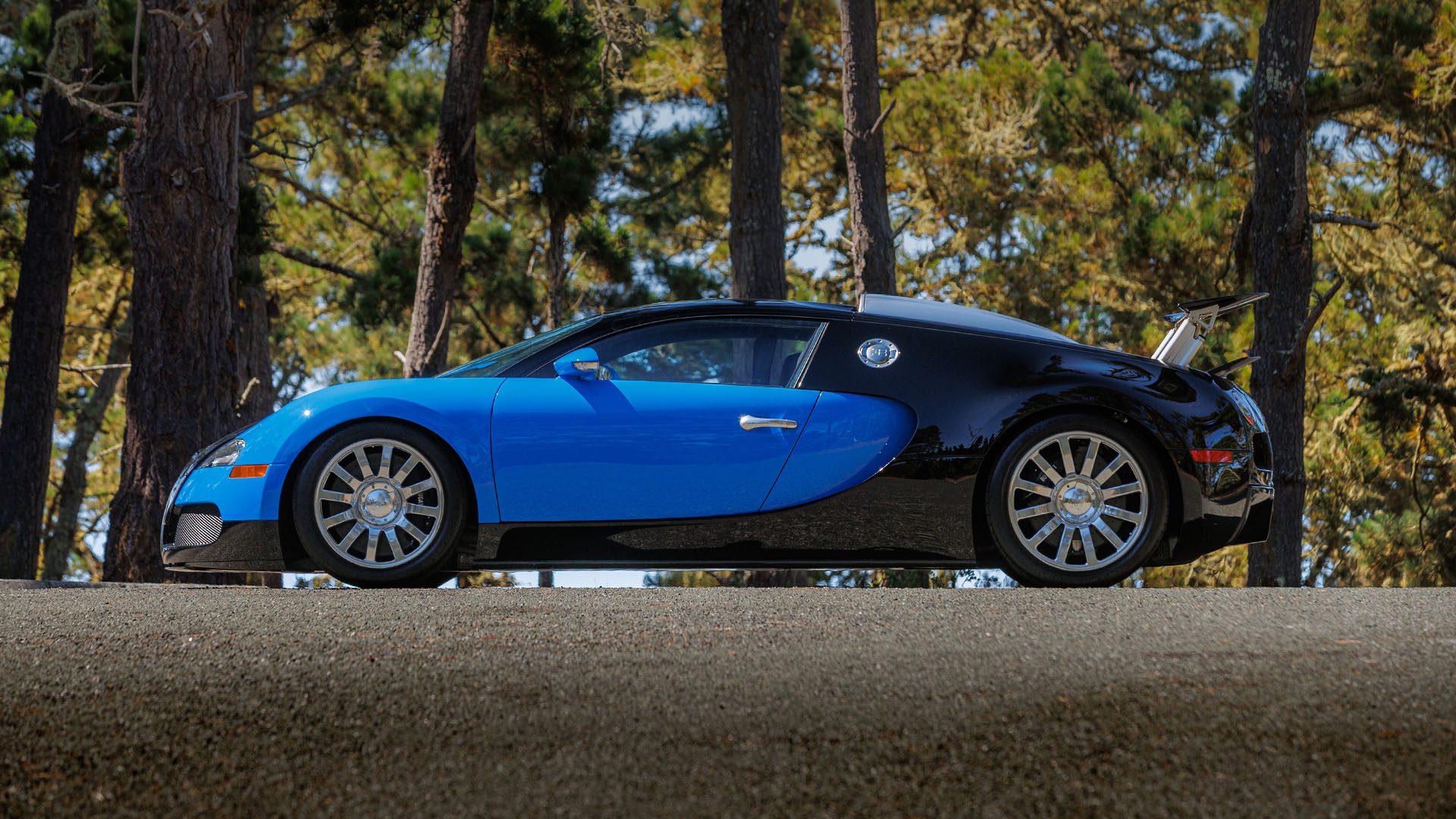 A blue and black Bugatti Veyron sports car is parked on a road with trees in the background, ready to impress at the Broad Arrow auction in Las Vegas 2025.