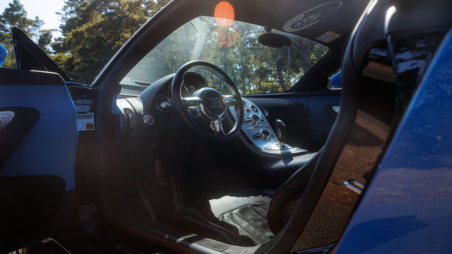 Interior view of a Bugatti Veyron luxury sports car, showcasing the steering wheel, dashboard, and driver’s seat with sunlight streaming through the open door—captured at Broad Arrow, Las Vegas 2025.