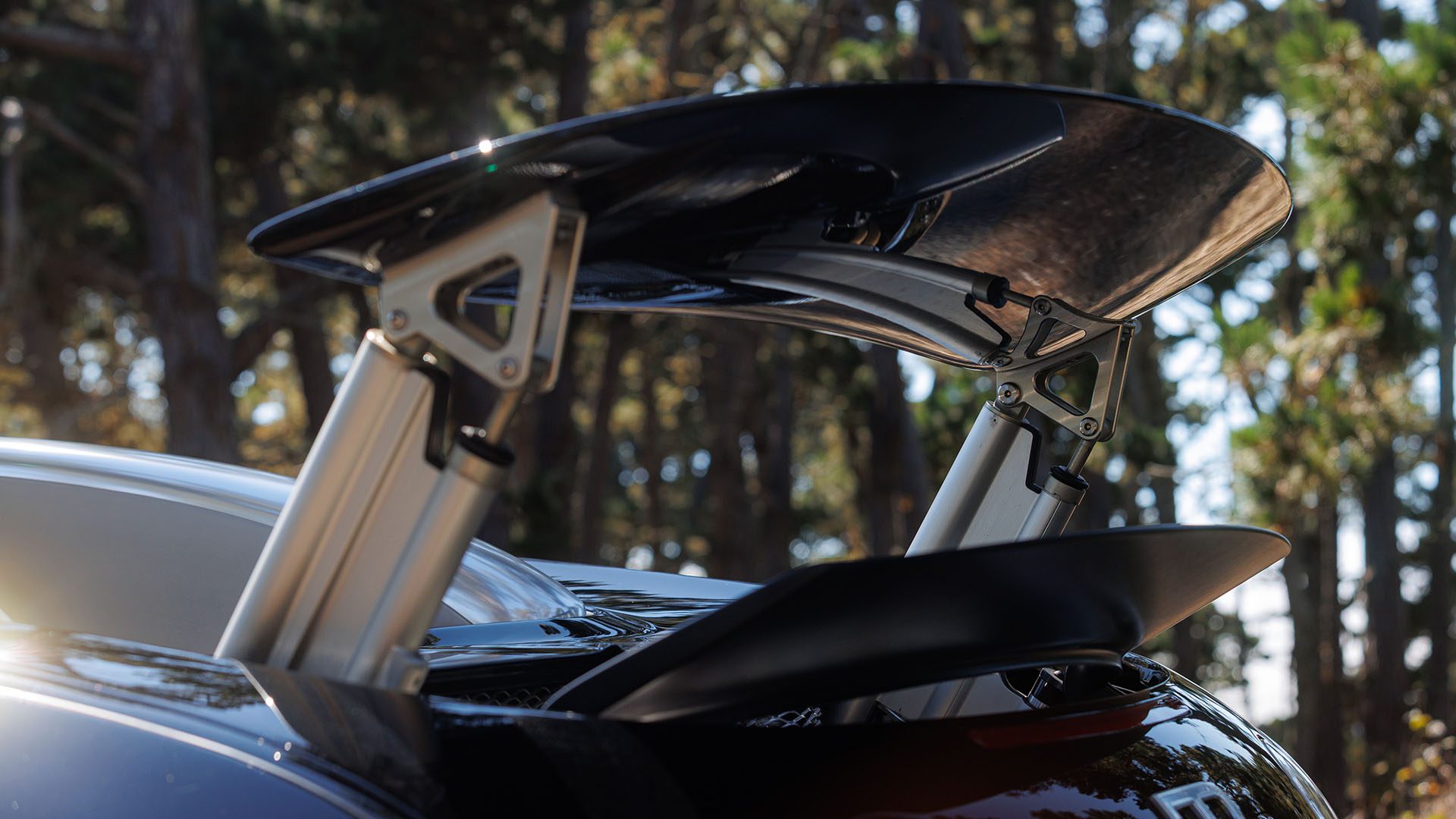 Close-up of an elevated rear spoiler on a Bugatti Veyron sports car, with a blurred background of trees—captured ahead of the Broad Arrow Las Vegas 2025 event.