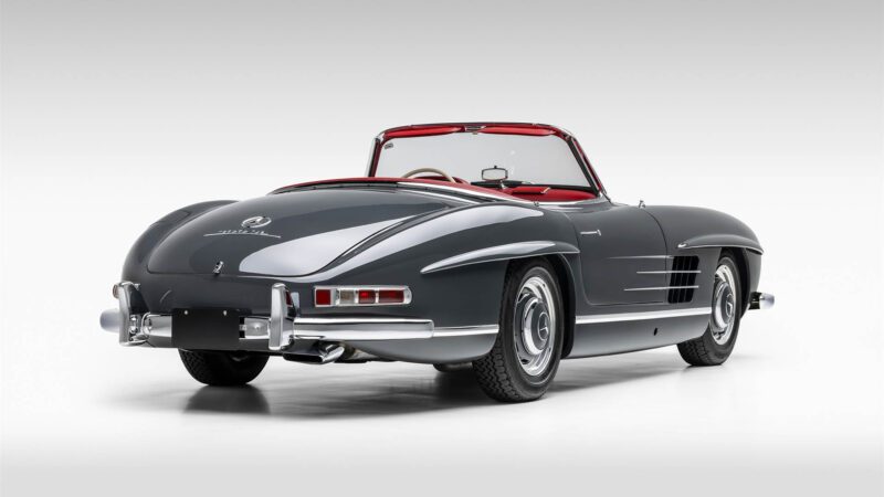 A classic Mercedes-Benz 300SL convertible in dark gray with a red interior, viewed from the rear against a plain light background, set to join the Broad Arrow auction at Las Vegas 2025.