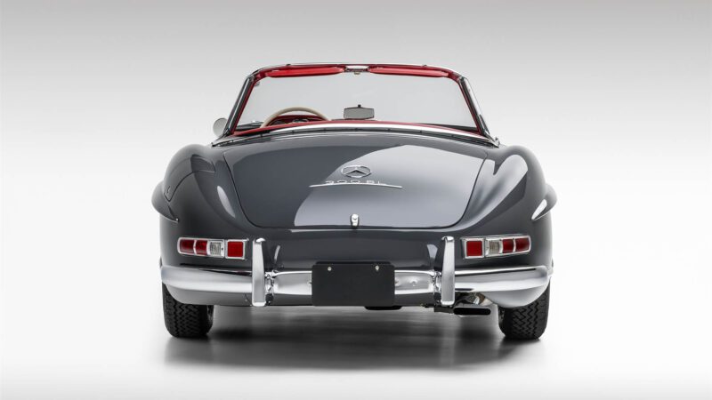 A rear view of a classic gray 2009 Mercedes-Benz SLR convertible with a red interior, showcasing its taillights, chrome bumper, and emblem against a plain background—highlighted for Broad Arrow Las Vegas 2025.