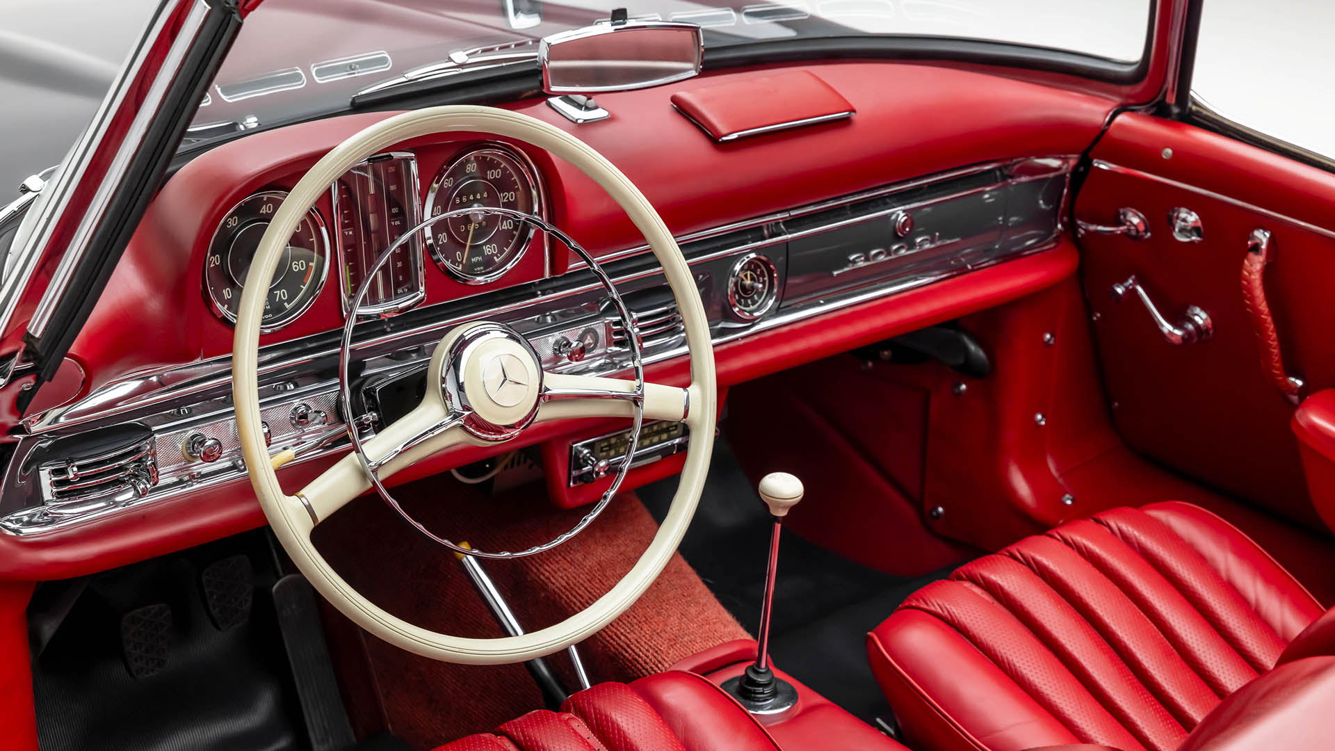 Interior of a classic red Mercedes-Benz SLR McLaren featuring a white steering wheel, analog gauges, manual gear shift, and red leather seats, reminiscent of automotive icons to be seen at Broad Arrow Las Vegas 2025.