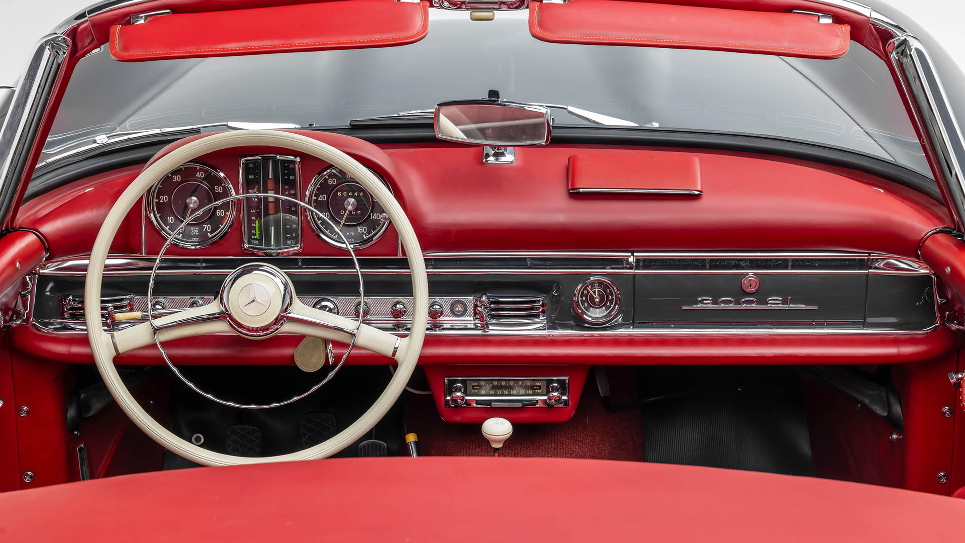 Interior view of a classic red Mercedes-Benz 300SL dashboard, featuring a white steering wheel and vintage gauges—an iconic design seen at events like Broad Arrow Las Vegas 2025, alongside legends like the Mercedes-Benz SLR McLaren.