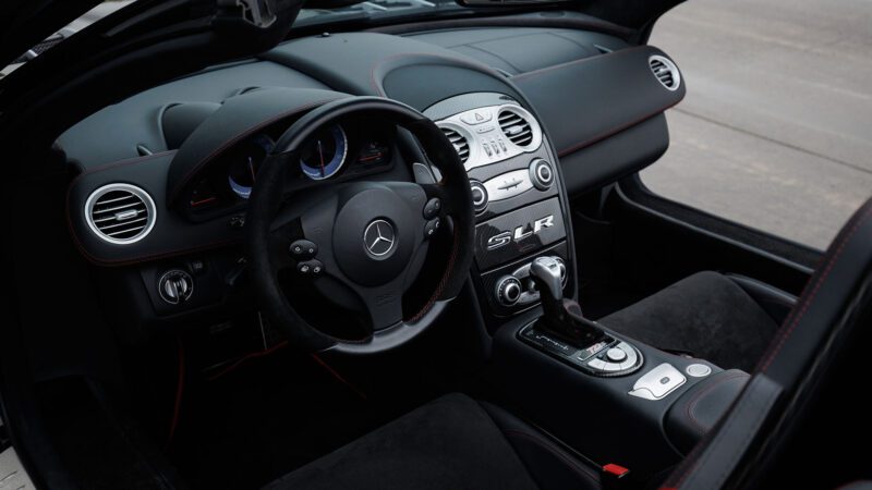 Interior view of a 2009 Mercedes-Benz SLR McLaren with black leather seats, red stitching, and a central console featuring various controls and an SLR logo. Featured at Broad Arrow Las Vegas 2025.