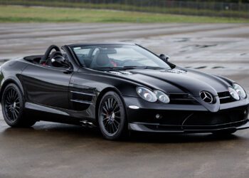 A 2009 Mercedes-Benz SLR McLaren convertible is parked on a wet concrete surface, with a grassy area and fence in the background, possibly awaiting its spotlight at Broad Arrow Las Vegas 2025.