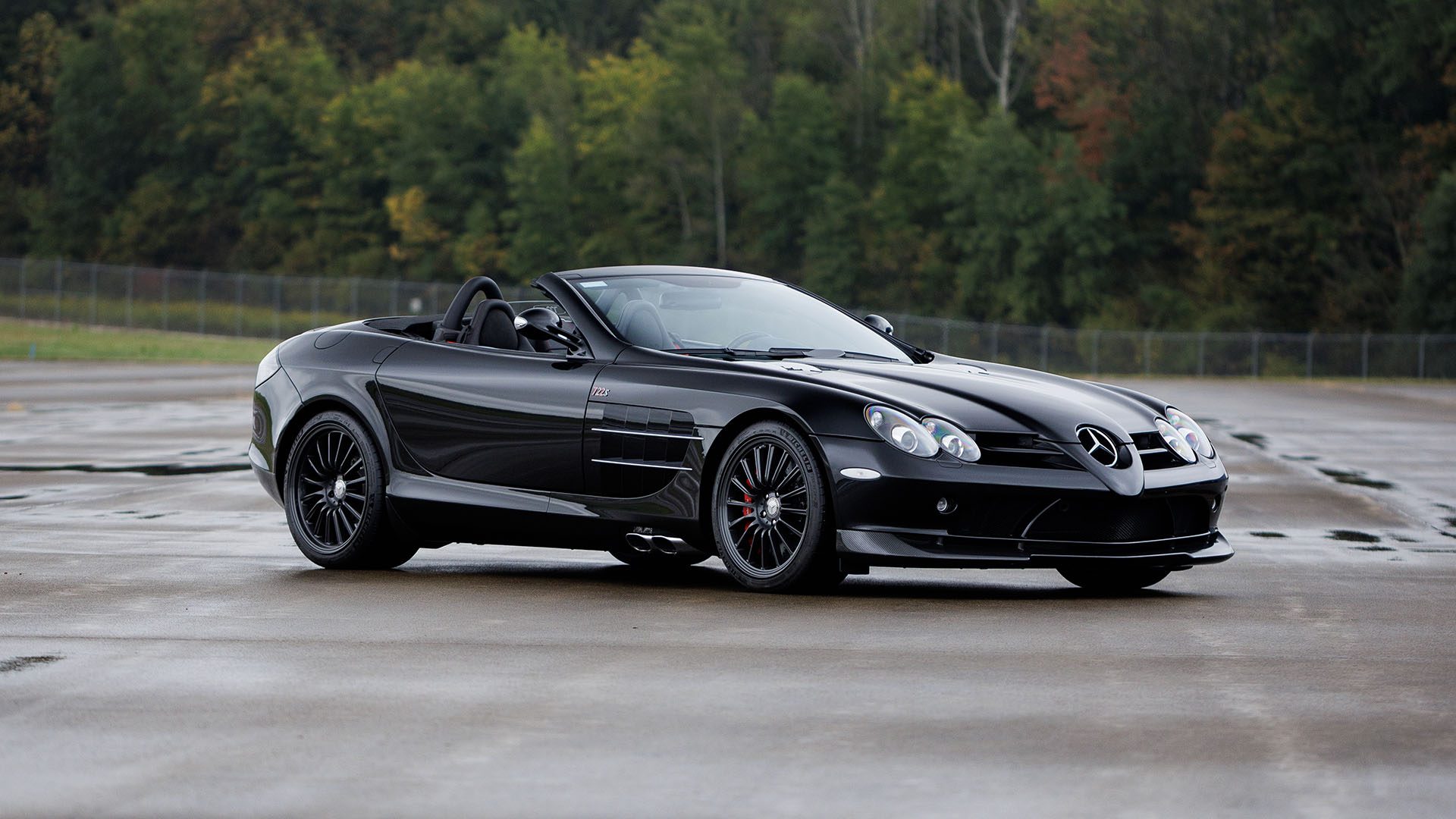 A 2009 Mercedes-Benz SLR McLaren convertible is parked on wet pavement with trees in the background, ready to impress at Broad Arrow Las Vegas 2025.