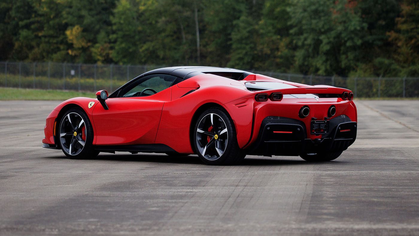 A red Ferrari sports car is parked on a paved surface, with trees and a wire fence visible in the background, evoking the excitement of a 2025 Preview at Broad Arrow Las Vegas.