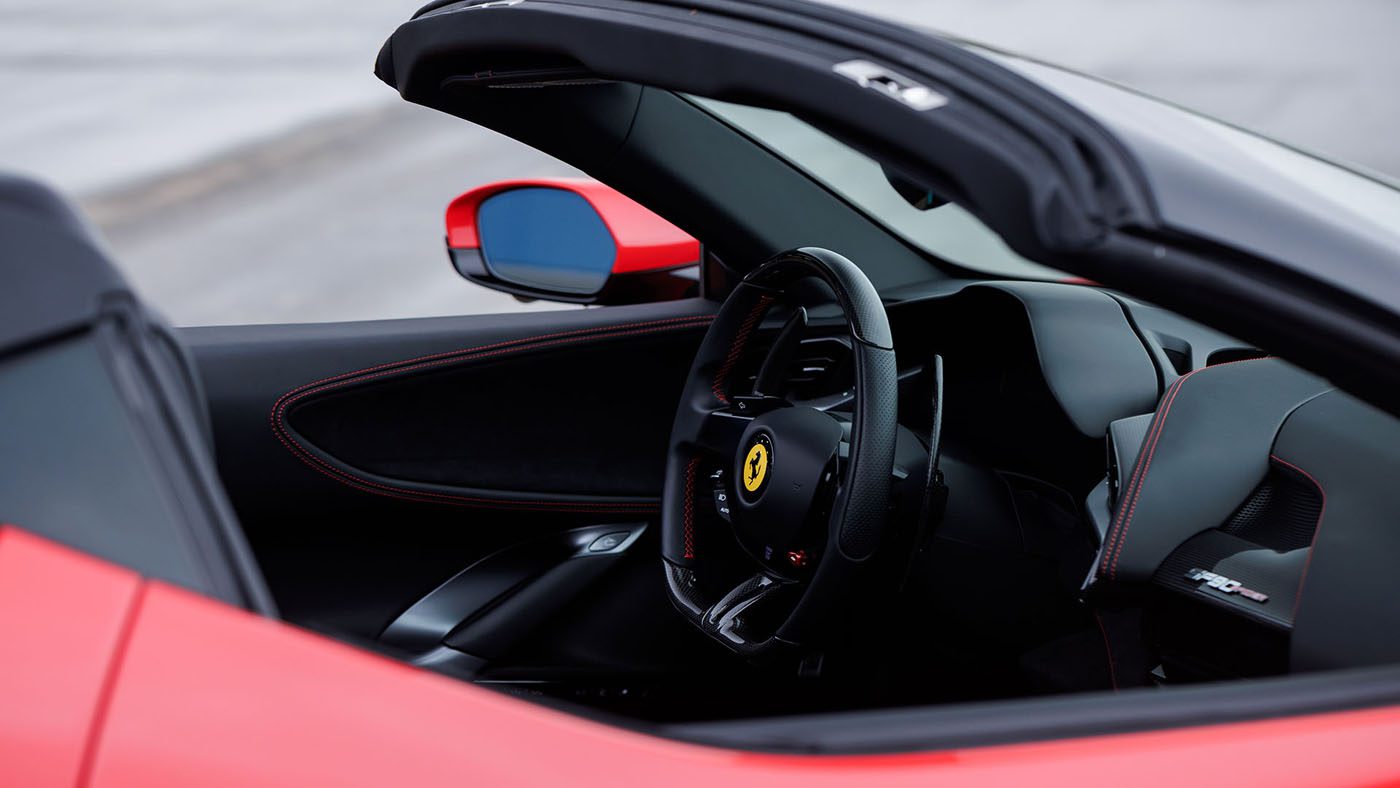 Close-up of the interior of a red convertible sports car, reminiscent of the luxury found in a 2010 Bugatti Veyron, showing the steering wheel with the Ferrari logo and black leather seats with red stitching.