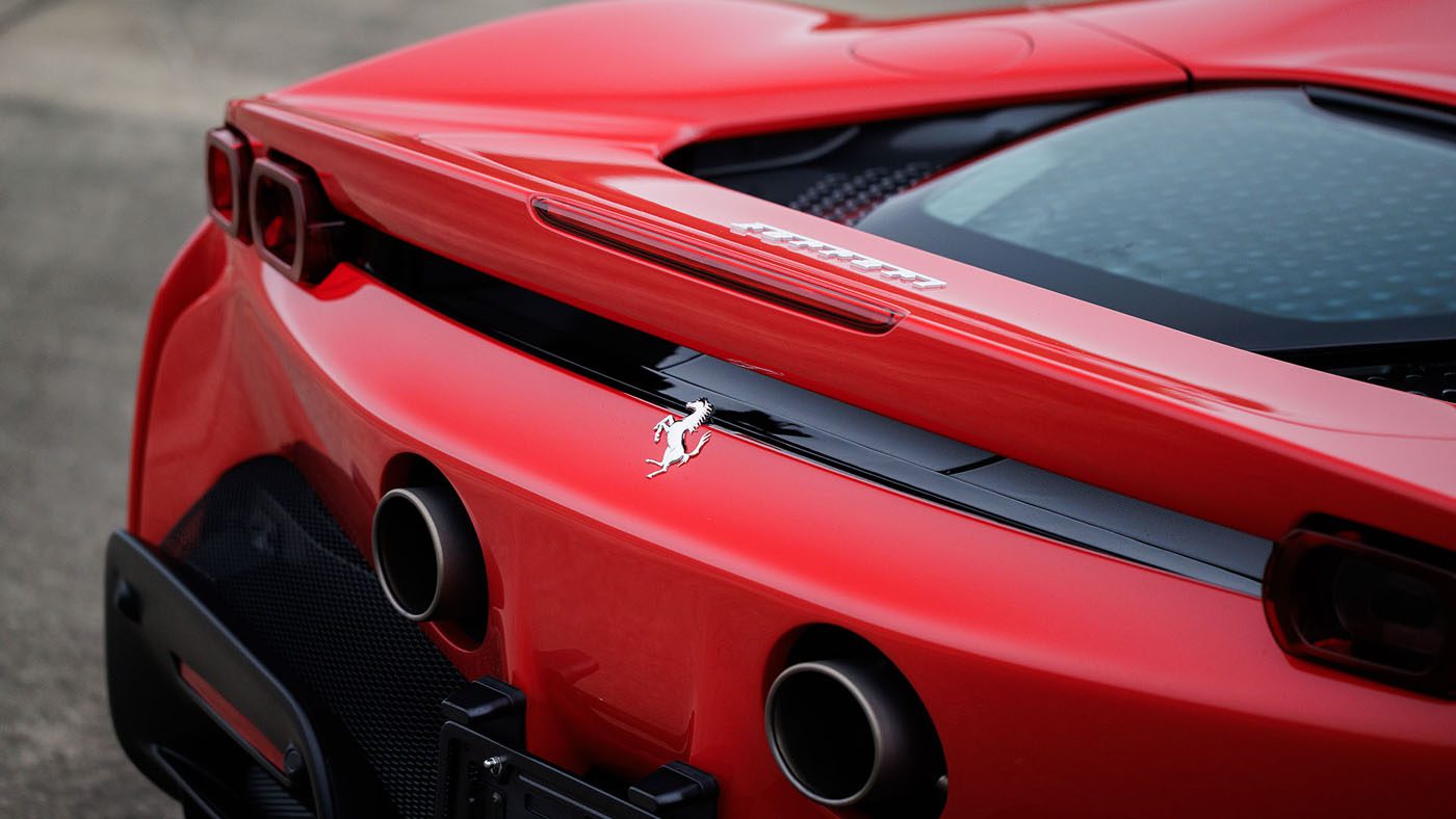 Close-up of the rear end of a red Ferrari sports car, showing dual exhaust pipes and the Ferrari emblem—soon to be showcased alongside a Bugatti Veyron at Broad Arrow, Las Vegas 2025.