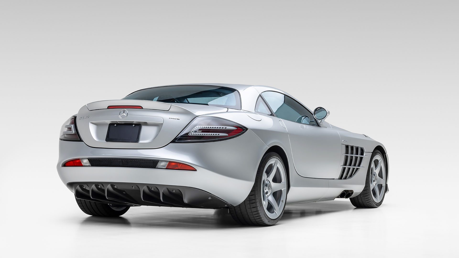 Rear view of a silver Mercedes-Benz SLR McLaren sports car, photographed on a plain white background, evoking the timeless elegance of the Mercedes-Benz 300 SL Roadster.