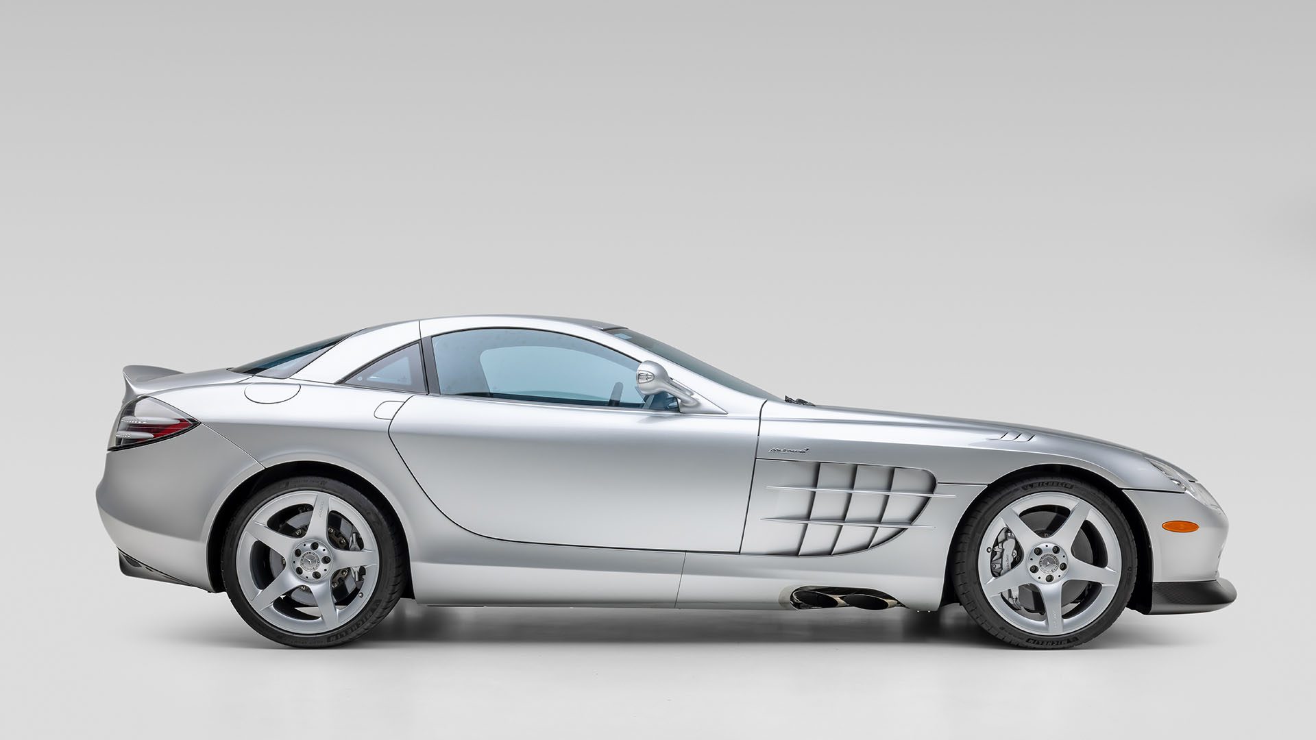 Side view of a silver Mercedes-Benz SLR McLaren sports car against a plain light gray background, set to feature at Broad Arrow’s Las Vegas 2025 event alongside classics like the Mercedes-Benz 300 SL Roadster.